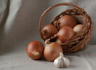 Onions in a basket and garlic on a background of natural fabric