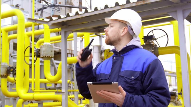 engineer holding a tablet, talking on walkie-talkie in modern industrial factory