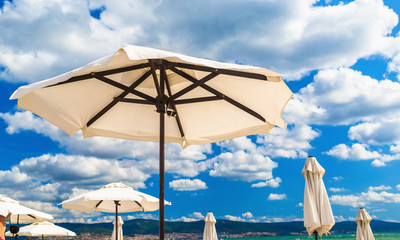 Big white parasols on a background of bright blue sky with cumulus clouds. Beach umbrellas. Shallow depth of field. Selective focus.