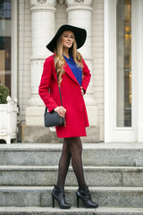 Young happy blonde woman in red coat walks on spring street