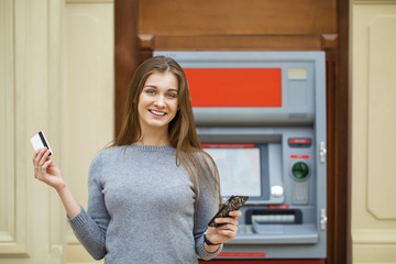 Young happy brunette woman withdrawing money from credit card at