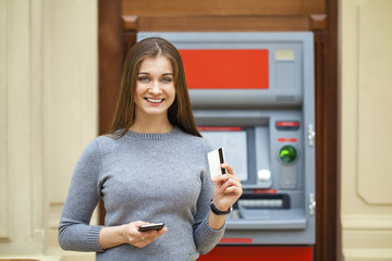 Fototapeta na wymiar Young happy brunette woman withdrawing money from credit card at