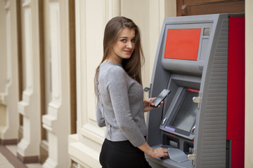 Fototapeta na wymiar Young happy brunette woman withdrawing money from credit card at