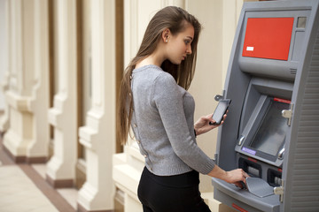 Young happy brunette woman withdrawing money from credit card at