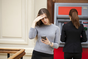 Frustrated young woman stands on against ATM
