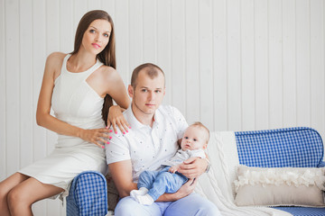 a young family with a nice and sweet little baby sitting on the sofa in a bright interior