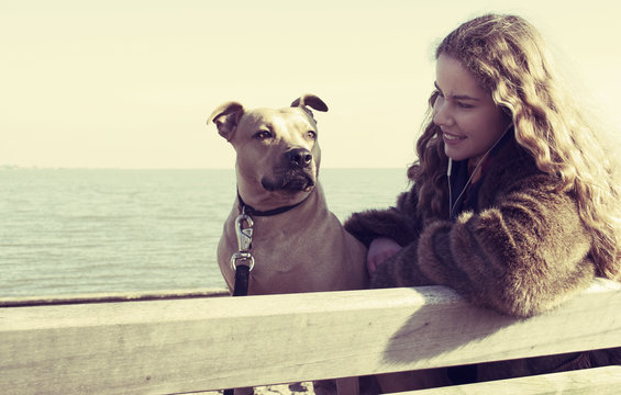 Knappe jonge vrouw zit buiten met haar hond op een bankje naar muziek te luisteren