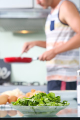 Lunch time! Man holding pan in the kitchen, green veggie in the foreground