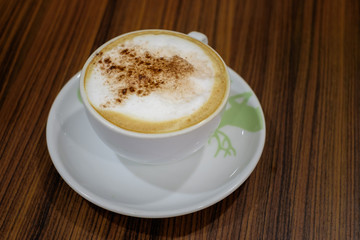 White cup containing hot cappuccino coffee on table