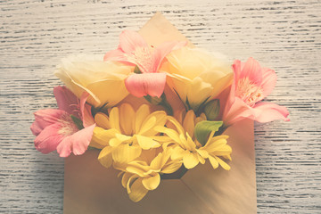 Bouquet of fresh flowers in envelope on wooden background