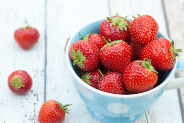 Fresh strawberries in a blue and white spotted mug. Small group of strawberries on the table beside the mug.