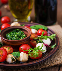 Caprese salad tomato and mozzarella with basil and herbs on a brown plate