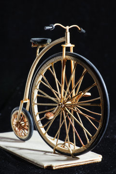 Wooden miniature of penny-farthing bicycle on black background. Old School bike with a big front wheel. Macro shot.