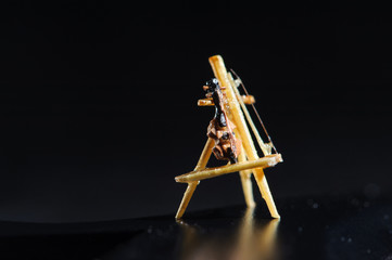 Wooden miniature of violin on black background. Violin standing on wooden stand. Macro shot.