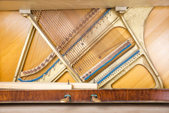 Bottom structure of an upright piano: pedals, metal frame with strings, bass and treble bridges.