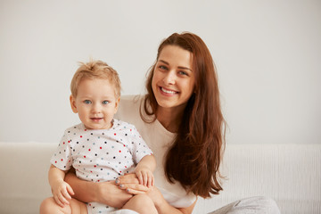 Young mother with her one years old little son dressed in pajamas are relaxing and playing in the...