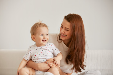 Young mother with her one years old little son dressed in pajamas are relaxing and playing in the...