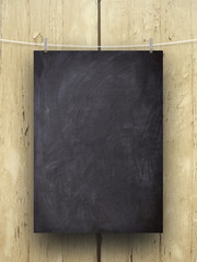 Close-up of one hanged blank blackboard sheet frame with pegs against brown wooden background