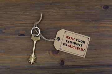 Key and a note on a wooden table with text - Want Your Company t