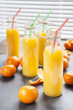 Natural and fresh orange juice in small bottles with fresh tangerine (mandarin)