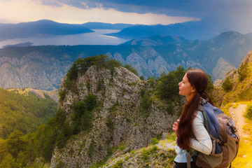 Woman traveler with backpack standing on big cliff in the mountains.