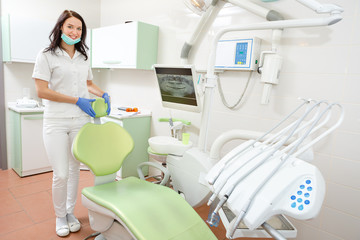 Portrait of a smiling young dentist woman leaning against dentist's chair in dental clinic