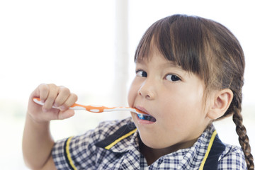 a school uniform little girl is brushing teeth