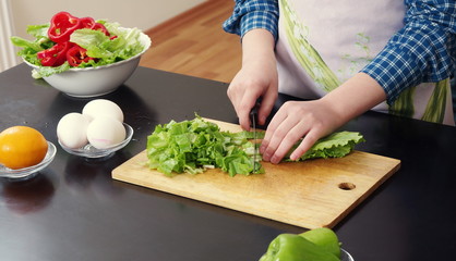 Little girl is cutting vegetables for salad closeup
