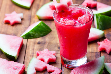 Glass of watermelon smoothie and pieces of watermelon on wooden background