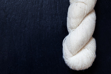 wei&szlig;es ungef&auml;rbtes Wollkn&auml;uel auf schwarzer Schieferplatte