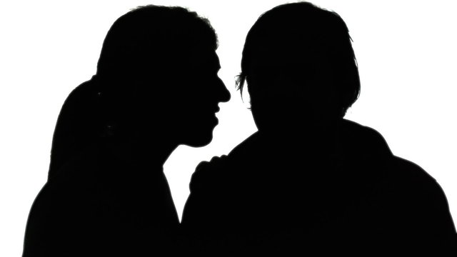 A woman whispering a secret in the ear of a man. Silhouette shot.
