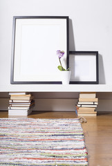 two black picture frames sitting on shelf with a flower in a jug