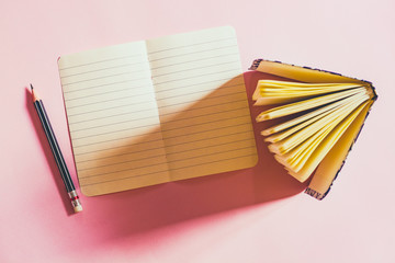 Paper sheet, notebook and pencil on pink paperboard, top view