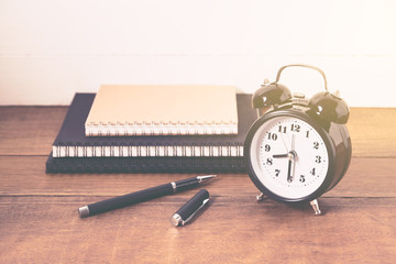 Clock with pen and notebook on wood table, still life