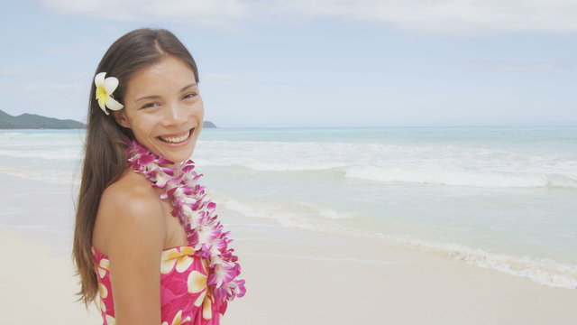 Woman on beach - smiling happy cheerful. Pretty female model wearing flower lei and sarong enjoying travel vacation holidays in sun. Beautiful mixed race Asian Caucasian girl on Hawaii, United States.