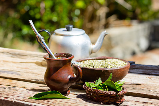 Herb mate (yerba mate) - traditional tea of Latin America. Herb mate in clay bowl, fresh herbs and kettle on old wooden background. Selective focus