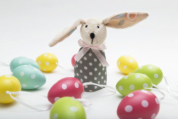 Easter bunny toy with dropping ear standing near colorful eggs