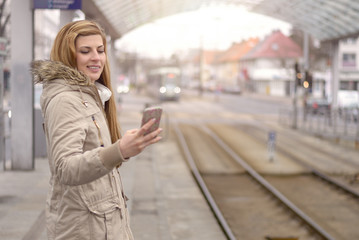 Frau mit Handy an einer Haltestelle