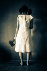 Mysterious girl in white dress standing in abandon house carrying an axe in front of the wall