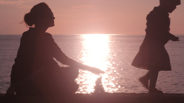Silhouettes of mom and little young girl are building a pyramid from pebble stones