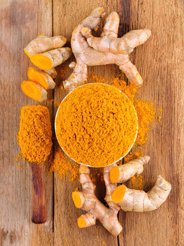 fresh turmeric roots with turmeric powder on wooden table