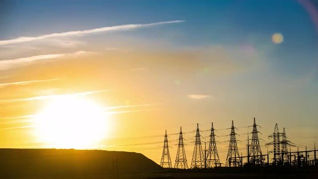 Sun going through electric high voltage pylon power transmission towers lines. Urban landscape. Electricity production and transportation, transmission. Time-lapse of sunset on a power plant.