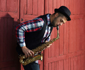 Young man playing on saxophone outside near the old wall
