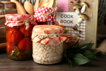 Jars with pickled vegetables, beans, spices and kitchenware on wooden background