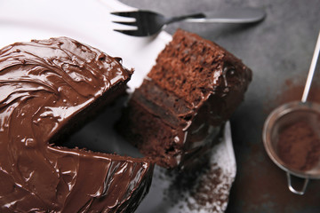 Chocolate cake on plate with a cut piece and fork and cocoa on gray background, closeup