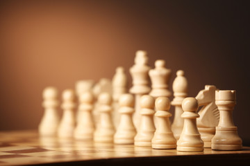 Chess pieces and game board on brown background