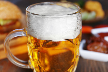 Glass mug of light beer with snacks on dark wooden table, close up