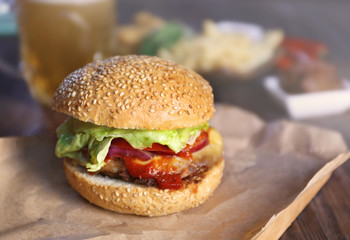 Big tasty hamburger on a paper with light beer in glass mug, close up