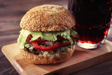 Glass mug of dark beer with hamburger on wooden table, close up