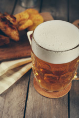 Glass of beer and chicken wings on wooden table, close up